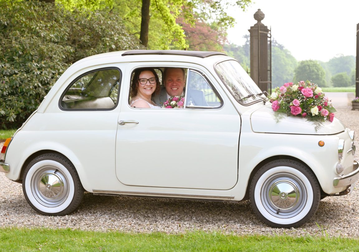 Fotocaroussel. Bruidspaar bij Huis Verwolde in Laren, stralend van geluk, in trouwauto met raam open.